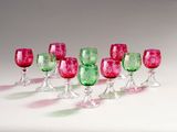 six red and green wine glasses lined up on a white surface