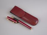 burgundy leather pen case with gold accents and a red ballpoint pen