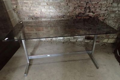 une table en verre avec un piètement en métal devant un mur de briques
