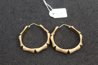 two pairs of gold hoop earrings on a black surface
