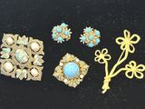 trois broches en or et turquoise et une paire de boucles d'oreilles posées sur un fond noir