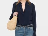 the model is wearing a black blouse and jeans with a straw bag