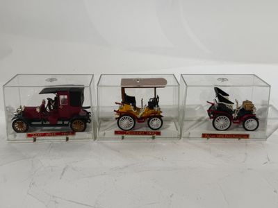 trois modèles réduits de voitures sont exposés dans une vitrine posée sur une surface blanche