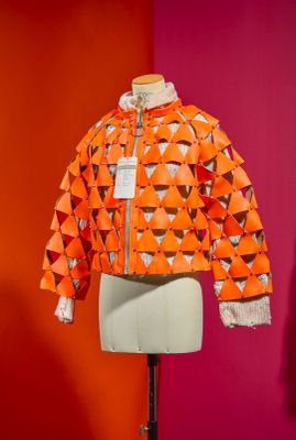 an orange jacket on a mannequin stand in front of a red wall
