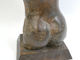 sculpture représentant un torse féminin sur un socle en bois, sur fond blanc