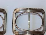 pair of silver metal buckles with beaded edges on a white surface