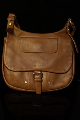 brown leather handbag sitting on a black surface with a black background