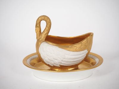 un canard doré et blanc posé sur une soucoupe, lui-même posé sur une soucoupe