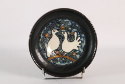 une assiette noire ornée de deux oiseaux, posée sur un socle