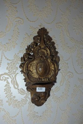 une horloge dorée accrochée au mur, à côté d'un mur recouvert de papier peint