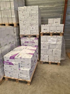 Plusieurs piles de cartons sont empilées sur des palettes dans un entrepôt