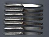 a set of six silverplated knives and a knife on a table