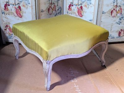 a yellow ottoman sitting on the floor in front of a wallpapered room