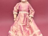 an old fashioned doll is sitting on a pink surface
