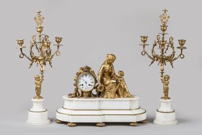 une horloge posée sur une table, à côté de trois chandeliers