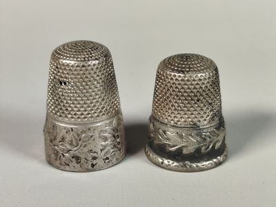 pair of silver thimbles on a white surface with a white background