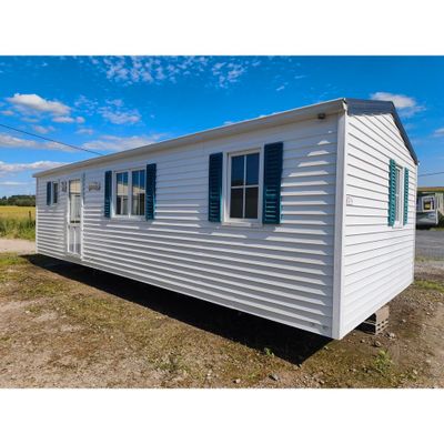 un mobil-home blanc posé au milieu d'un champ de terre battue