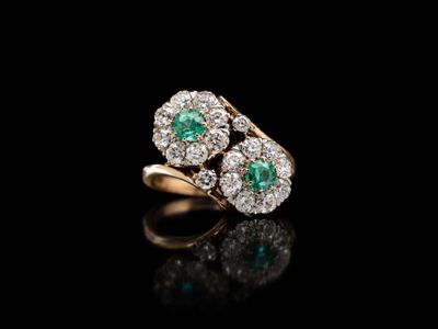 an emerald and diamond ring on a black surface