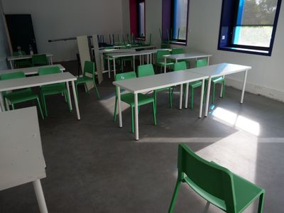 tables and chairs in an empty classroom with bright windows