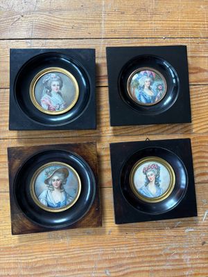 quatre portraits miniatures de femmes, encadrés dans des cadres noirs, posés sur un plancher en bois