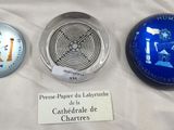 trois objets en verre sont exposés sur un tissu blanc, accompagnés d'une étiquette portant leur nom