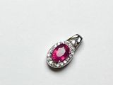 un gros plan d'un pendentif en rubis et diamants posé sur une surface blanche