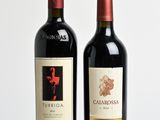 two bottles of red wine sitting on top of a wooden table