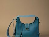 sac à main en cuir bleu avec une bandoulière, sur fond beige