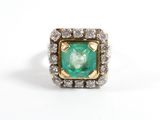 une photo d'une bague sertie d'une émeraude et de diamants posée sur une surface blanche