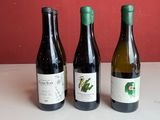 trois bouteilles de vin posées sur une table, avec un mur rouge en arrière-plan