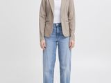 a woman in a beige blazer and jeans stands in front of a white background