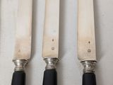 four knives are lined up on a table with a white table cloth