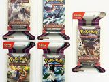 Trois paquets de cartes à collectionner Pokémon sont exposés sur une surface blanche.
