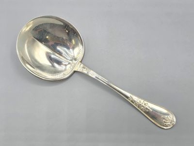 an antique silver spoon with a handle on a white surface