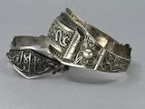 pair of silver bracelets on a table with a white background