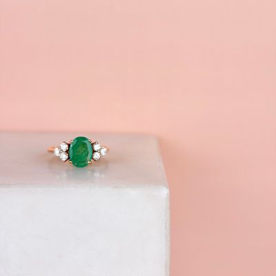 a close up of a green emerald and diamond ring on a pink background