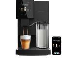 a black coffee machine with a glass of milk next to it
