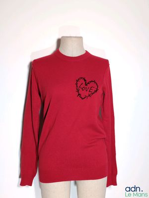 Le pull est rouge et il y a un cœur noir dessus.