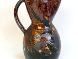 a brown and black vase sitting on a white surface