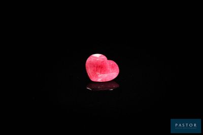 un gros plan sur une pierre rose en forme de cœur posée sur une surface noire