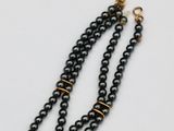 a close up of a black beaded necklace with a gold clasp