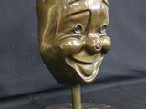 brass statue of a smiling face on a marble base with a black background