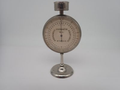 une horloge en argent posée sur un socle, sur une surface blanche
