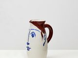cruche en céramique blanche ornée d'un visage bleu et d'une anse marron sur fond blanc