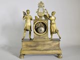 a gold clock that has three people on it