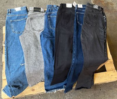 Plusieurs paires de jeans sont empilées sur une palette dans un entrepôt