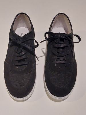 une paire de baskets noires à semelles blanches posées sur une surface blanche