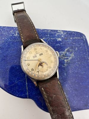 an old watch with a brown leather strap sitting on top of a blue marble slab