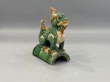 une figurine verte et dorée représentant un chat assis sur un rocher
