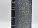 an old book with a black cover sitting on top of a white surface